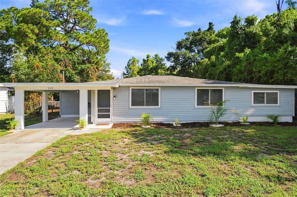 A single-story house with light blue siding, a carport, and a front lawn — 660 DEXTER DRIVE, DUNEDIN, FL