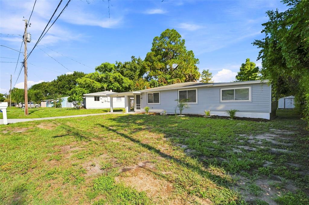 A single-story house with light gray siding and a large front yard under a blue sky — 660 DEXTER DRIVE, DUNEDIN, FL