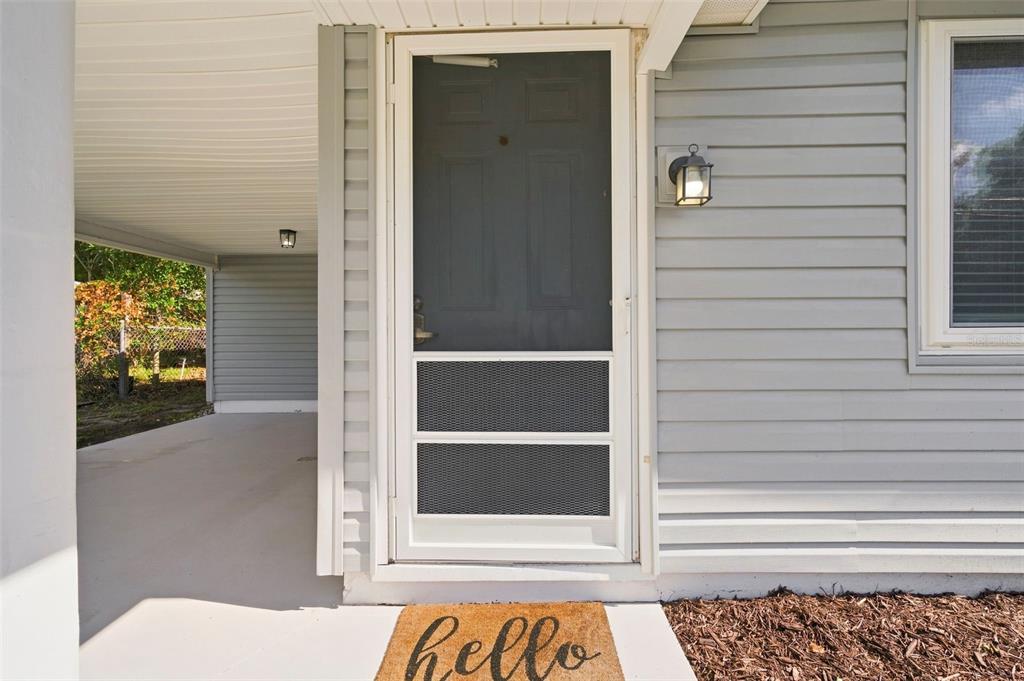 A front entryway features a white screen door, light gray siding, and a hello doormat — 660 DEXTER DRIVE, DUNEDIN, FL