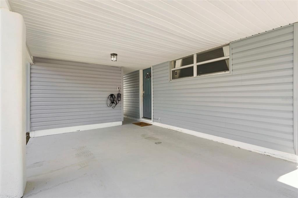 A covered carport with light gray siding, a concrete floor, and a blue front door — 660 DEXTER DRIVE, DUNEDIN, FL