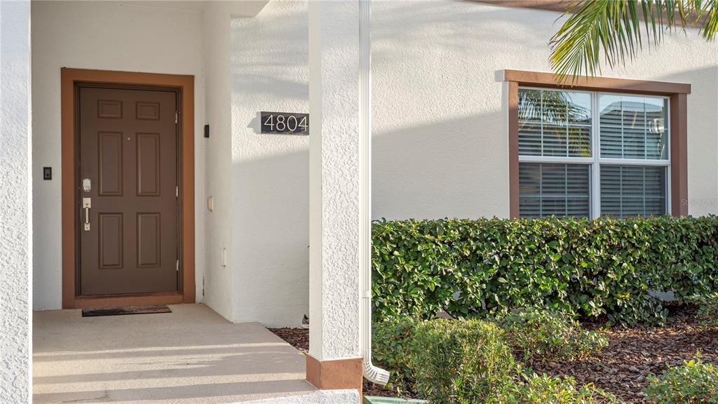 The exterior of a house features a brown front door, a house number, and landscaping — 4804 LULLABY LANE, KISSIMMEE, FL