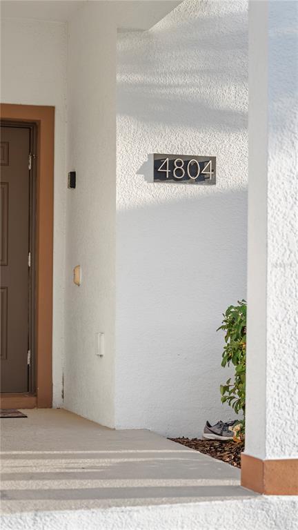 A view of a home entrance with a brown door, white stucco walls, and house numbers — 4804 LULLABY LANE, KISSIMMEE, FL
