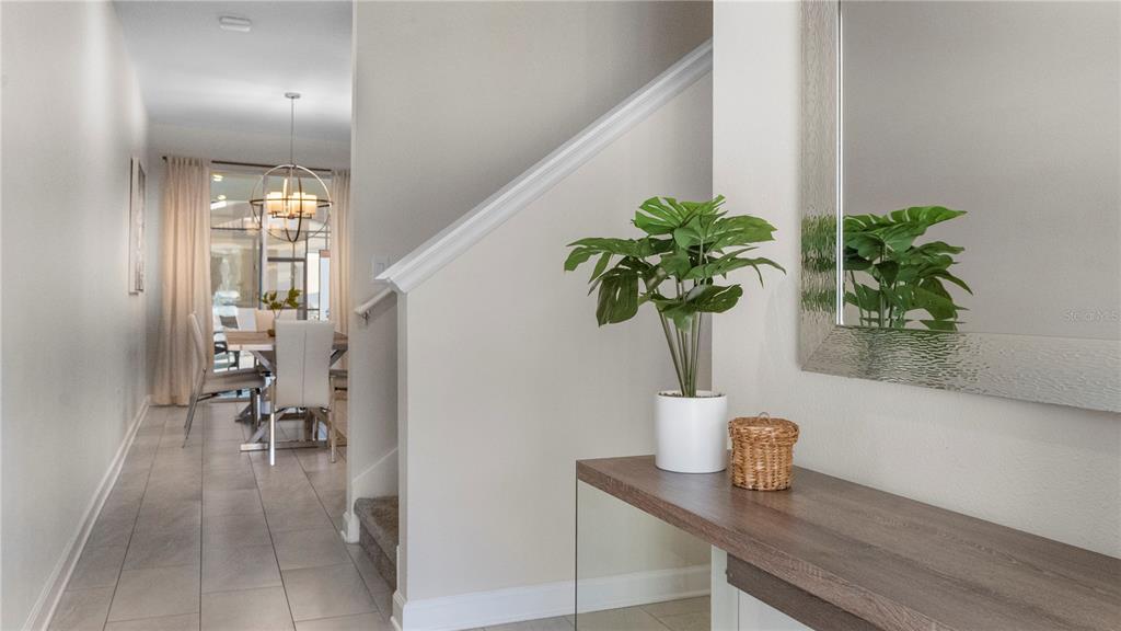 A hallway with tile flooring leads to a dining area past a staircase and console table — 4804 LULLABY LANE, KISSIMMEE, FL