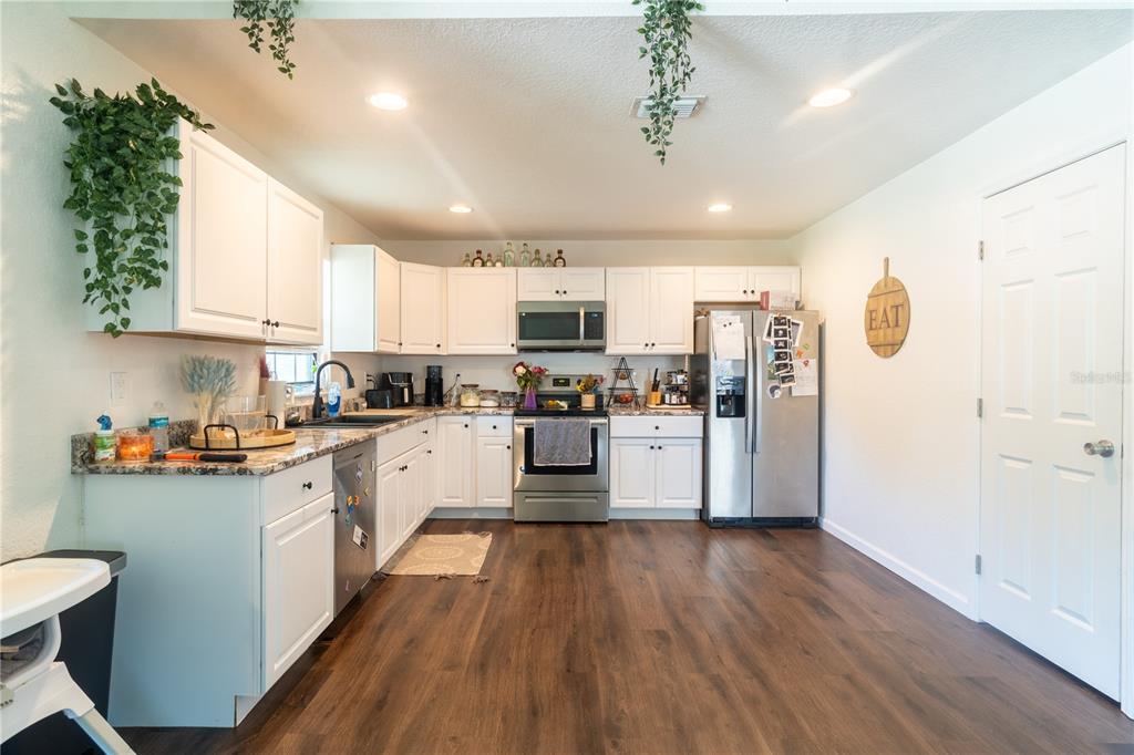 A kitchen features white cabinets, stainless steel appliances, granite countertops, and dark wood-look flooring — 146 8TH STREET, WINTER HAVEN, FL