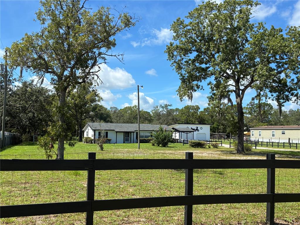 A white house and detached garage sit behind a black wooden fence on a grassy lot — 17620 CHORVAT AVENUE, SPRING HILL, FL
