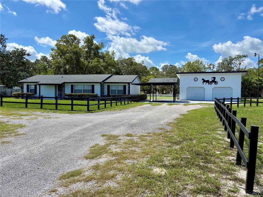 A single-story house with a gravel driveway, black fencing, and a detached two-car garage — 17620 CHORVAT AVENUE, SPRING HILL, FL