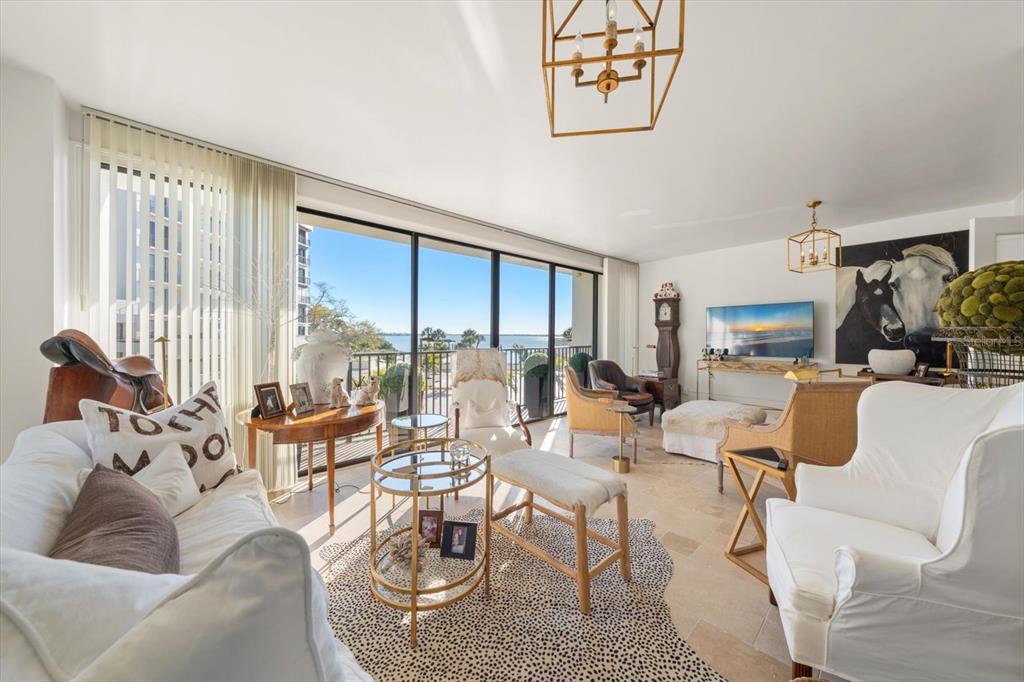 A bright living room features white furniture, a patterned rug, and floor-to-ceiling windows overlooking water — 8 BELLEVIEW BOULEVARD UNIT 203, BELLEAIR, FL