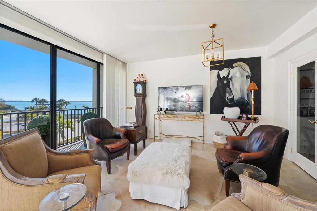 A living room features leather armchairs, a white ottoman, a television, and a balcony view — 8 BELLEVIEW BOULEVARD UNIT 203, BELLEAIR, FL