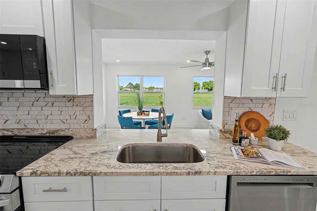 A kitchen with white cabinets, granite countertops, and a view into a dining area — 9975 41ST STREET N, PINELLAS PARK, FL