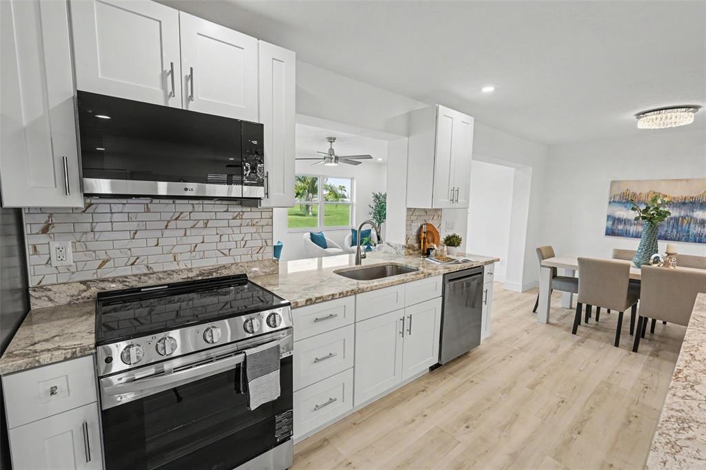 A modern kitchen features white cabinets, granite countertops, stainless steel appliances, and light wood flooring — 9975 41ST STREET N, PINELLAS PARK, FL
