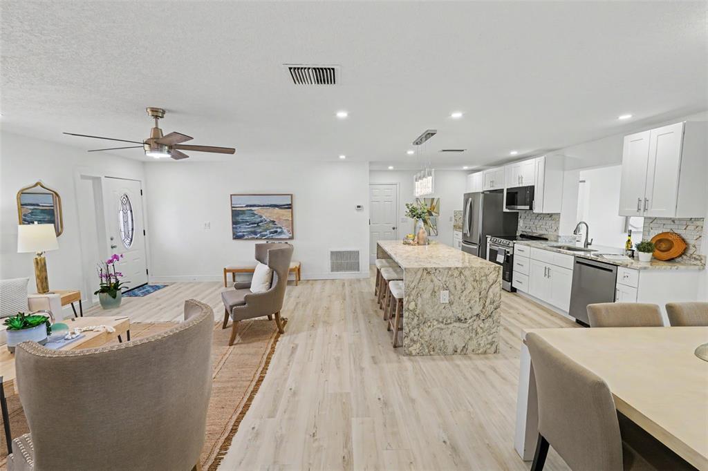 An open-concept kitchen and living area features white cabinetry, granite countertops, and light wood flooring — 9975 41ST STREET N, PINELLAS PARK, FL