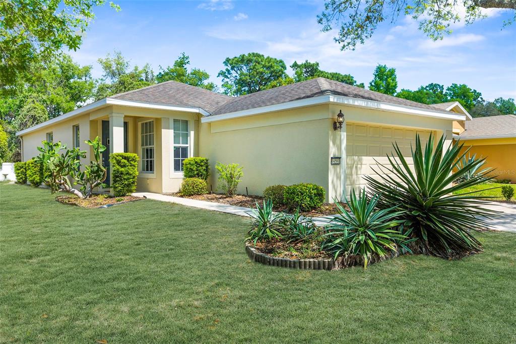 A single-story yellow house with a two-car garage and a landscaped front yard — 14581 WAKE ROBIN DRIVE, BROOKSVILLE, FL