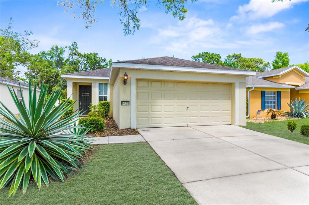 A single-story house with a beige stucco exterior, a two-car garage, and a front lawn — 14581 WAKE ROBIN DRIVE, BROOKSVILLE, FL