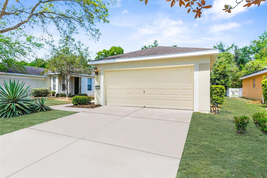 A beige single-story house features a two-car garage, a concrete driveway, and a landscaped yard — 14581 WAKE ROBIN DRIVE, BROOKSVILLE, FL