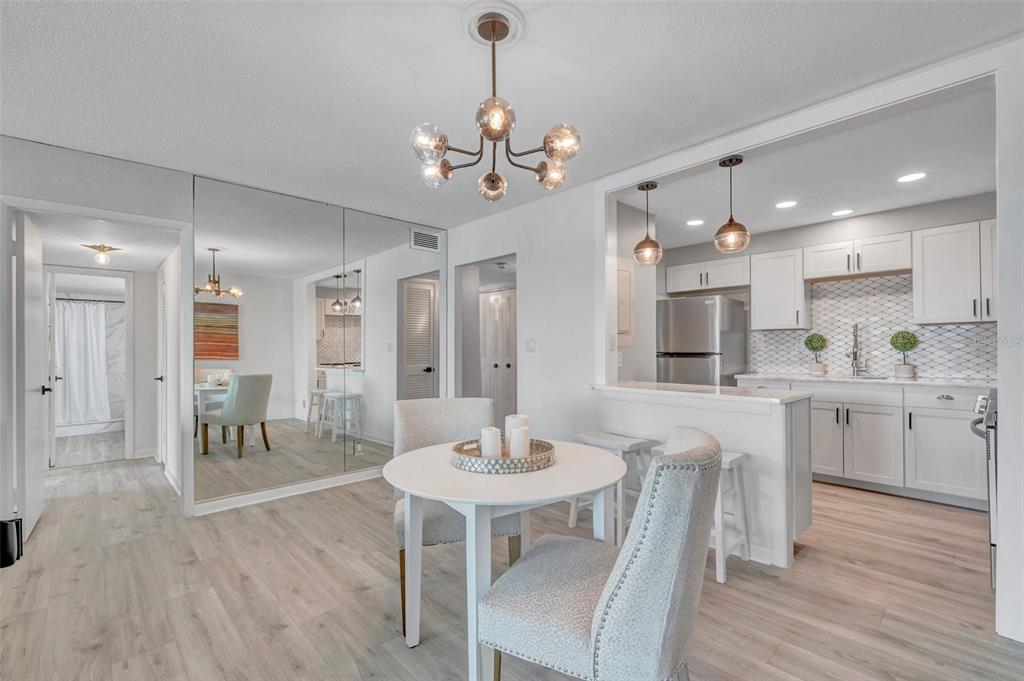 A dining area with a round table and mirrored wall opens into a white kitchen — 400 64TH AVENUE UNIT 907 W, ST PETE BEACH, FL