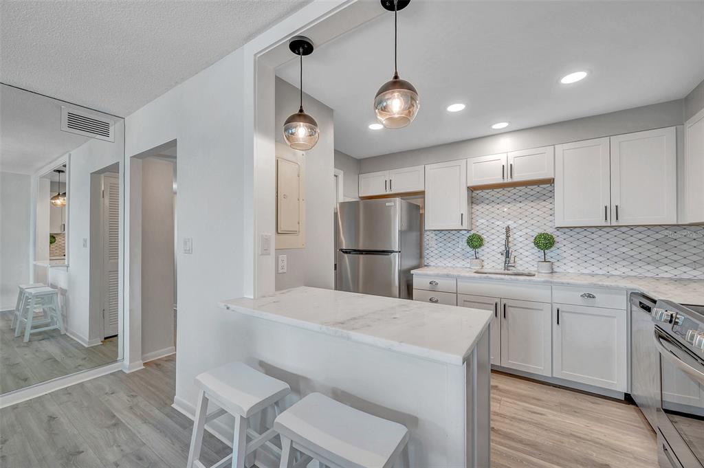 A kitchen features white cabinets, stainless steel appliances, a marble-topped breakfast bar, and pendant lighting — 400 64TH AVENUE UNIT 907 W, ST PETE BEACH, FL