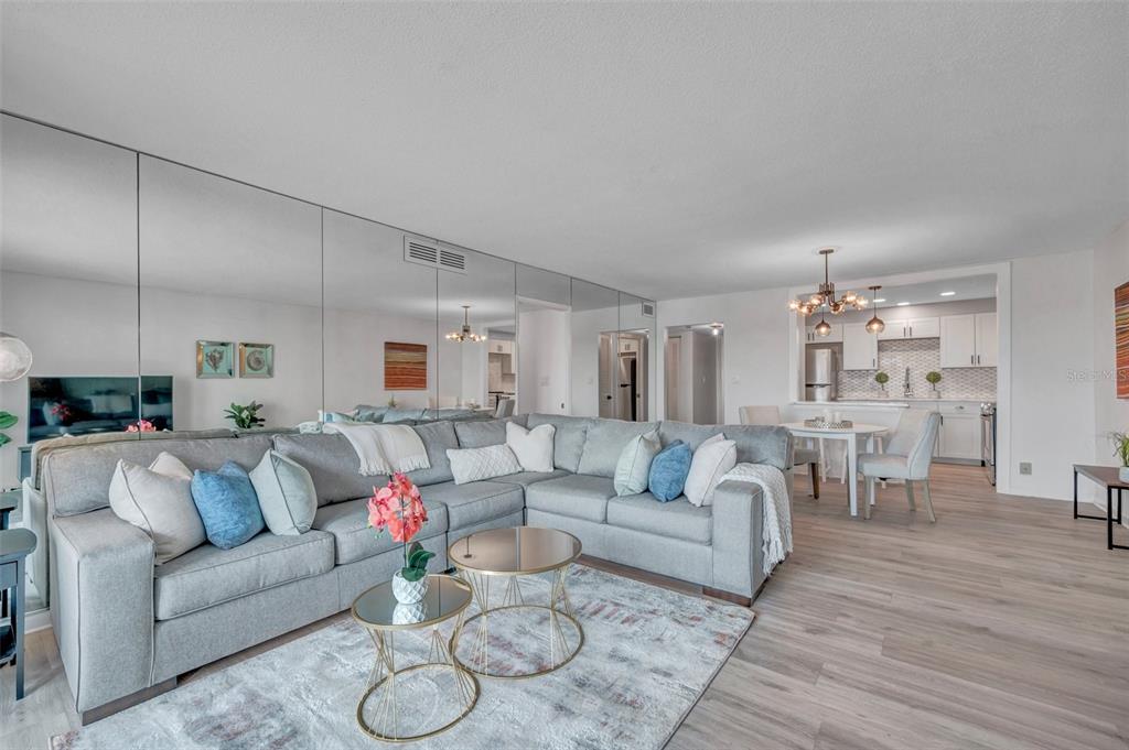 A living room with a large gray sectional sofa, mirrored wall, and adjacent dining area — 400 64TH AVENUE UNIT 907 W, ST PETE BEACH, FL