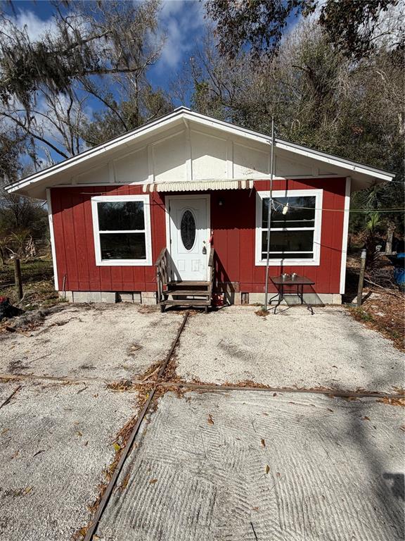 A small, red, single-story house with a white front door and a gravel driveway — 1211 NW EUCALYPTUS AVENUE, ARCADIA, FL