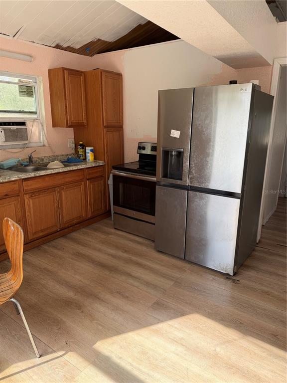 A kitchen features wood cabinets, a stainless steel refrigerator, a stove, and light wood flooring — 1211 NW EUCALYPTUS AVENUE, ARCADIA, FL