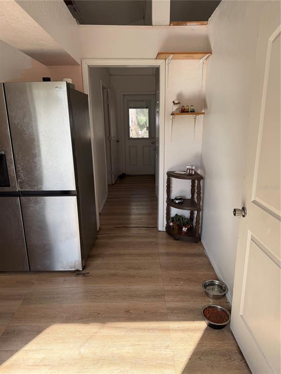 A stainless steel refrigerator stands in a hallway with wood-look flooring and a corner shelf — 1211 NW EUCALYPTUS AVENUE, ARCADIA, FL