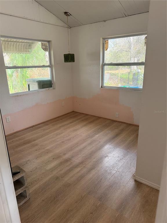 An unfinished room with light wood-look flooring, two windows, and walls partially painted white — 1211 NW EUCALYPTUS AVENUE, ARCADIA, FL