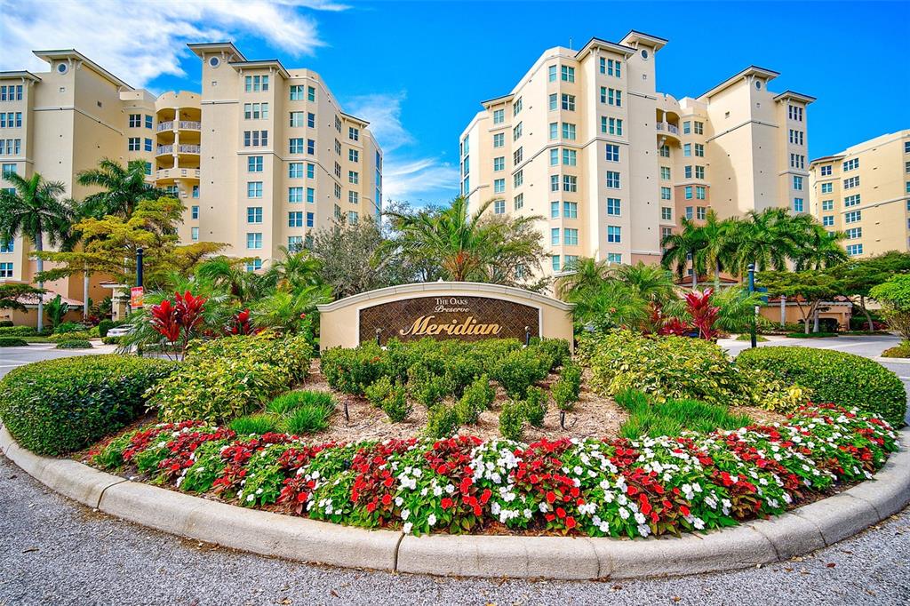 A landscaped entrance sign for The Oaks Preserve Meridian sits before two large apartment buildings — 385 N POINT ROAD UNIT 402, OSPREY, FL