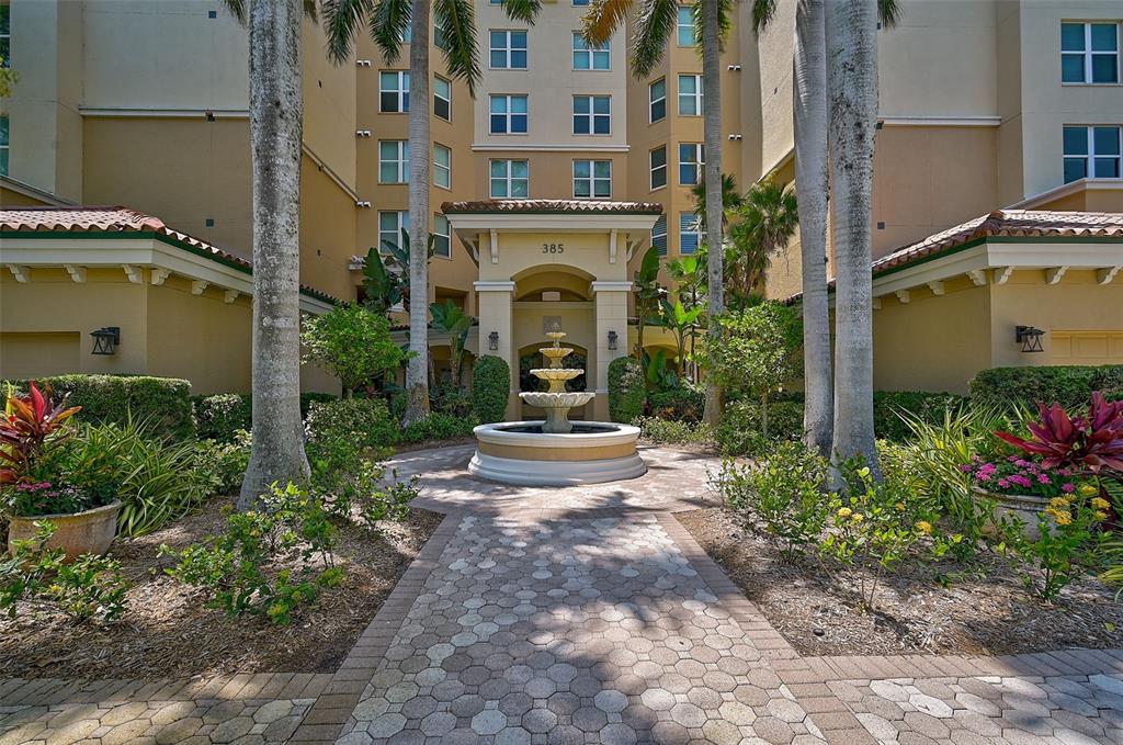 A multi-story building entrance features a central tiered fountain and a paved stone walkway — 385 N POINT ROAD UNIT 402, OSPREY, FL