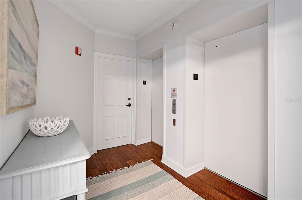 A hallway with hardwood floors, a white console table, and an elevator with a number four — 385 N POINT ROAD UNIT 402, OSPREY, FL