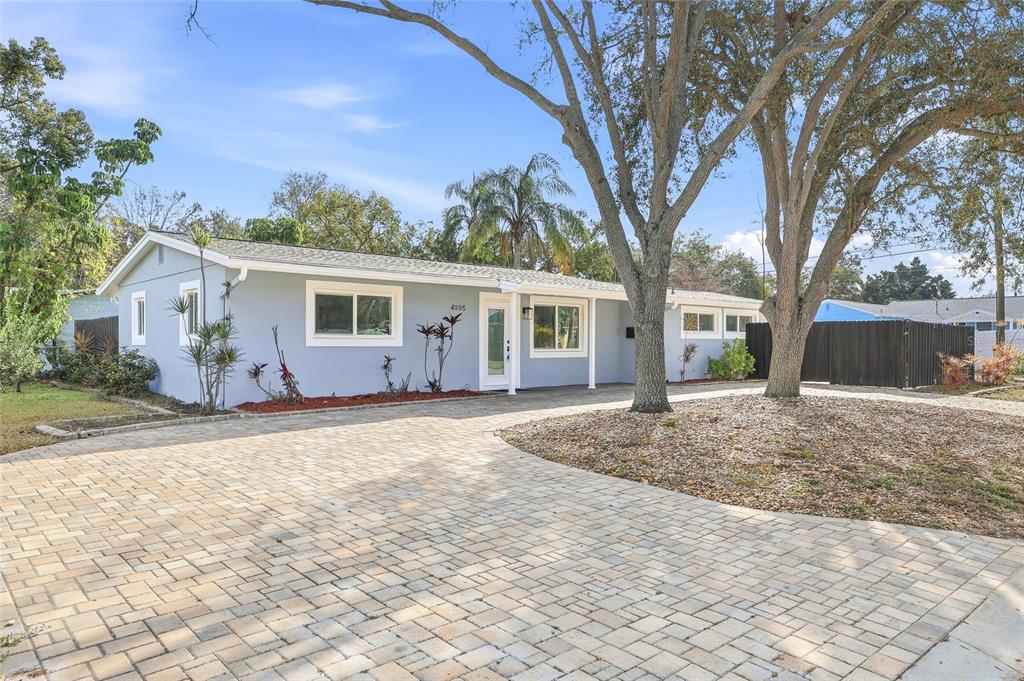 A light blue single-story house features a paved driveway and mature trees in the front yard — 4095 LOCUST STREET NE, ST PETERSBURG, FL
