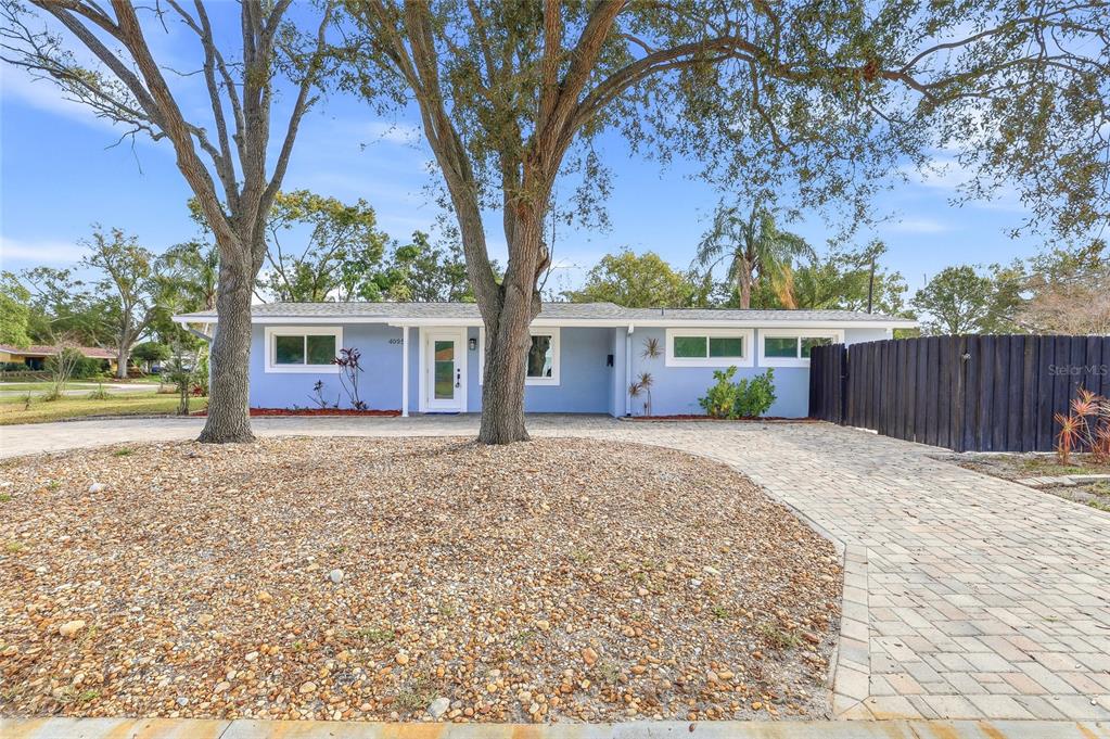A light blue single-story house features a paved driveway and two large trees in front — 4095 LOCUST STREET NE, ST PETERSBURG, FL