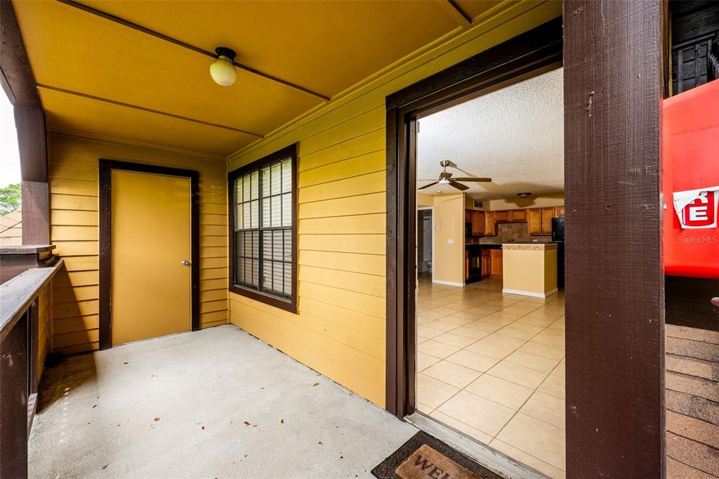 A covered balcony with yellow siding leads into an interior kitchen with tiled flooring — 420 FORESTWAY CIRCLE UNIT 206, ALTAMONTE SPRINGS, FL