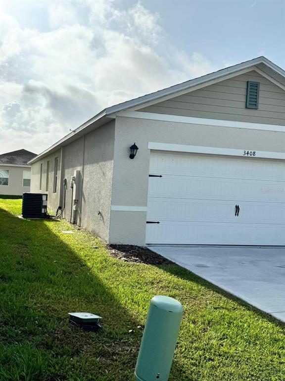 The exterior of a single-story house features a white garage door and beige stucco siding — 3408 COSTELLO CIRCLE, WINTER HAVEN, FL