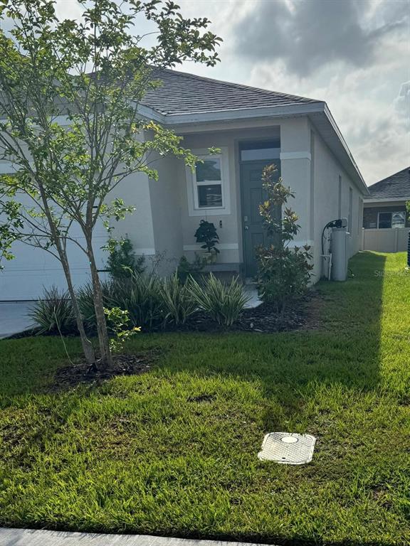 A single-story house exterior features a gray front door, a small tree, and landscaping — 3408 COSTELLO CIRCLE, WINTER HAVEN, FL