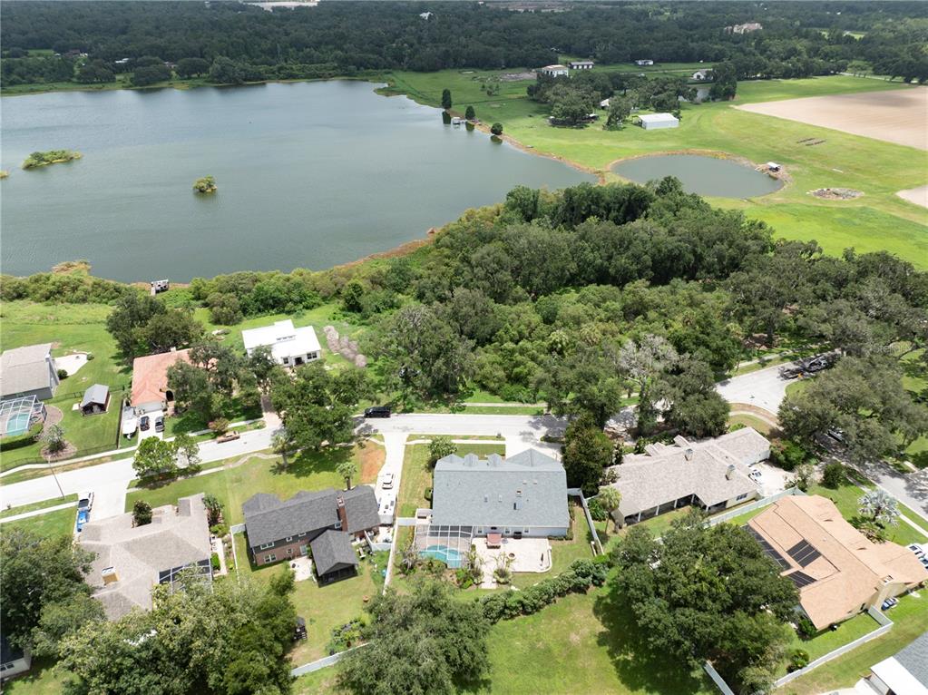 An aerial view shows several houses with pools near a large lake and wooded area — 504 COVINGTON PARK STREET, SEFFNER, FL