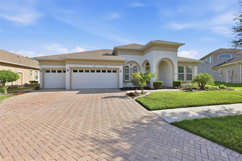 A single-story house features a paved driveway, a three-car garage, and a covered entryway — 7121 HATPIN LOOP, WESLEY CHAPEL, FL