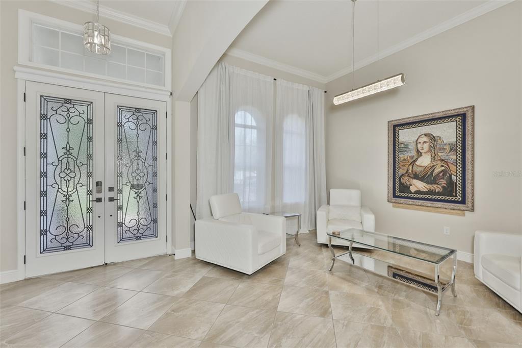 A bright entryway features white tile floors, two white armchairs, a glass coffee table, and art — 7121 HATPIN LOOP, WESLEY CHAPEL, FL