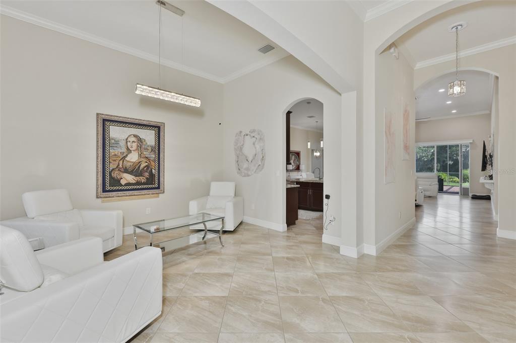 A bright living area features white armchairs, a glass coffee table, and tile flooring — 7121 HATPIN LOOP, WESLEY CHAPEL, FL
