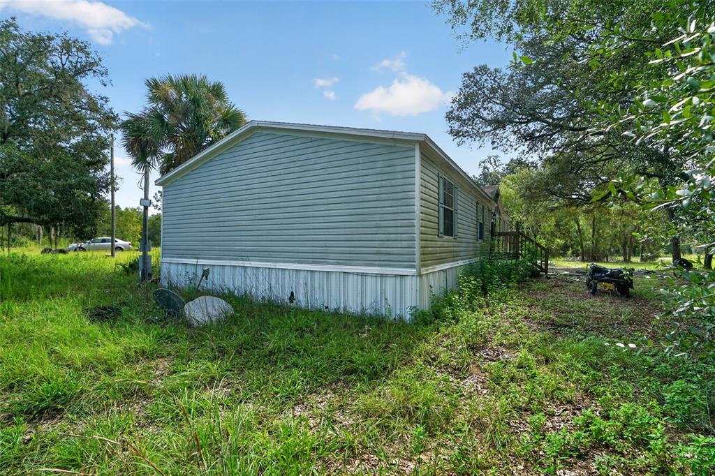 An exterior view of a light green mobile home with white skirting and overgrown grass — 8351 NE 106TH STREET, BRONSON, FL