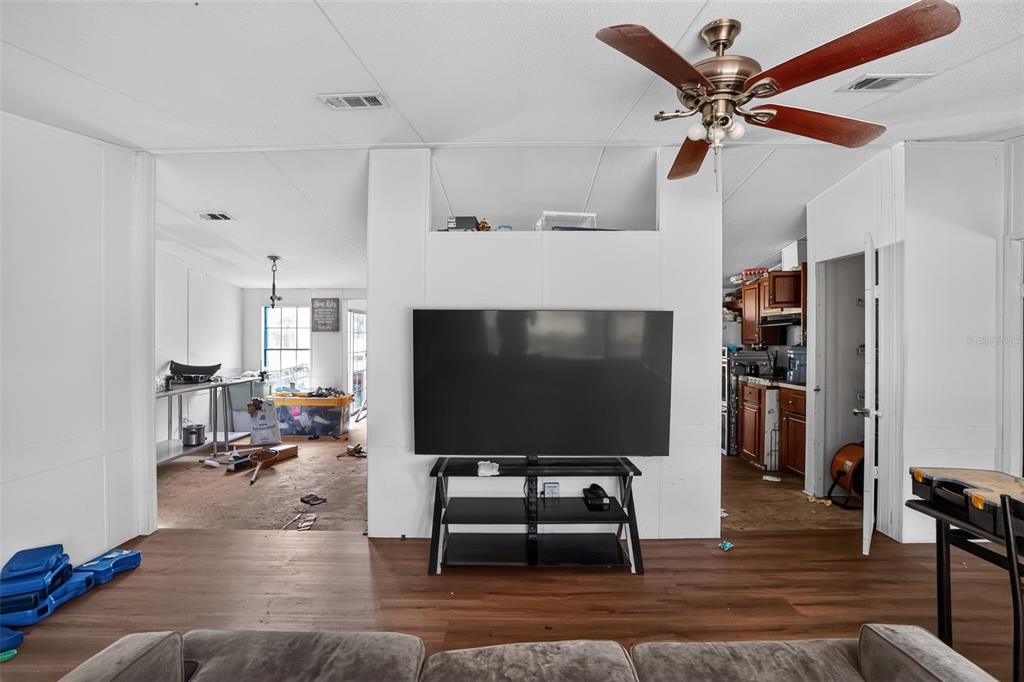 A living room features a large television on a stand, wood-look flooring, and a ceiling fan — 8351 NE 106TH STREET, BRONSON, FL