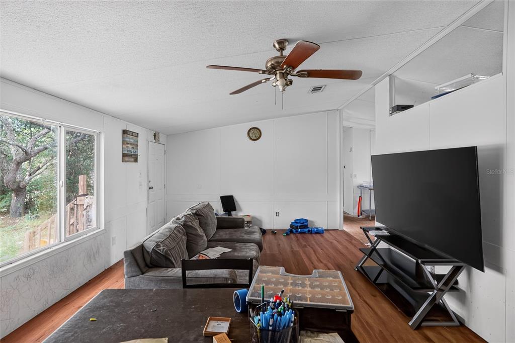 A living room features wood-look flooring, a gray sofa, a ceiling fan, and a television — 8351 NE 106TH STREET, BRONSON, FL