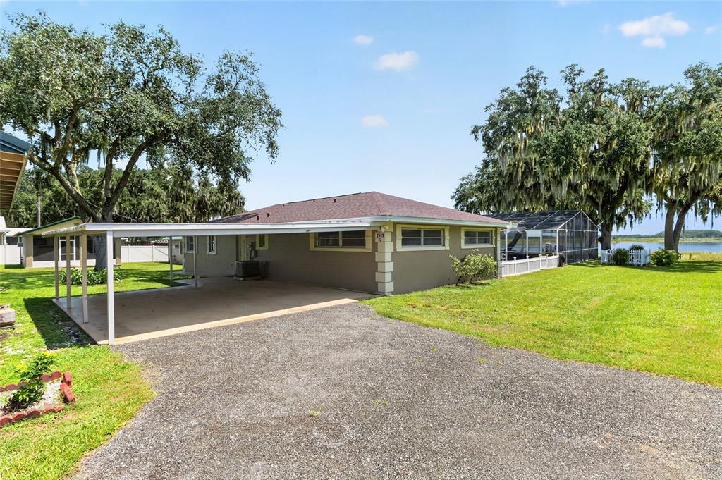 A single-story house with a gravel driveway, attached carport, and large trees in the yard — 2489 N LAKEFRONT DRIVE, HERNANDO, FL