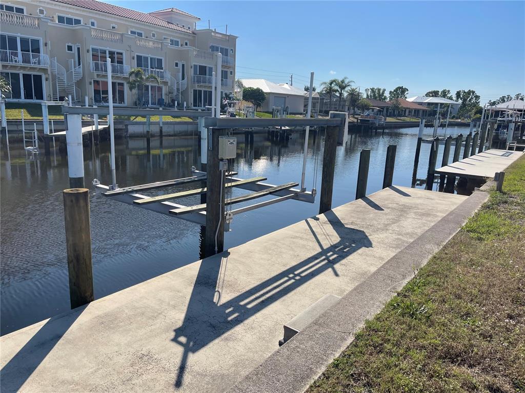 A boat lift sits in a canal next to a concrete dock and residential buildings — 1336 MEDITERRANEAN DRIVE, PUNTA GORDA, FL
