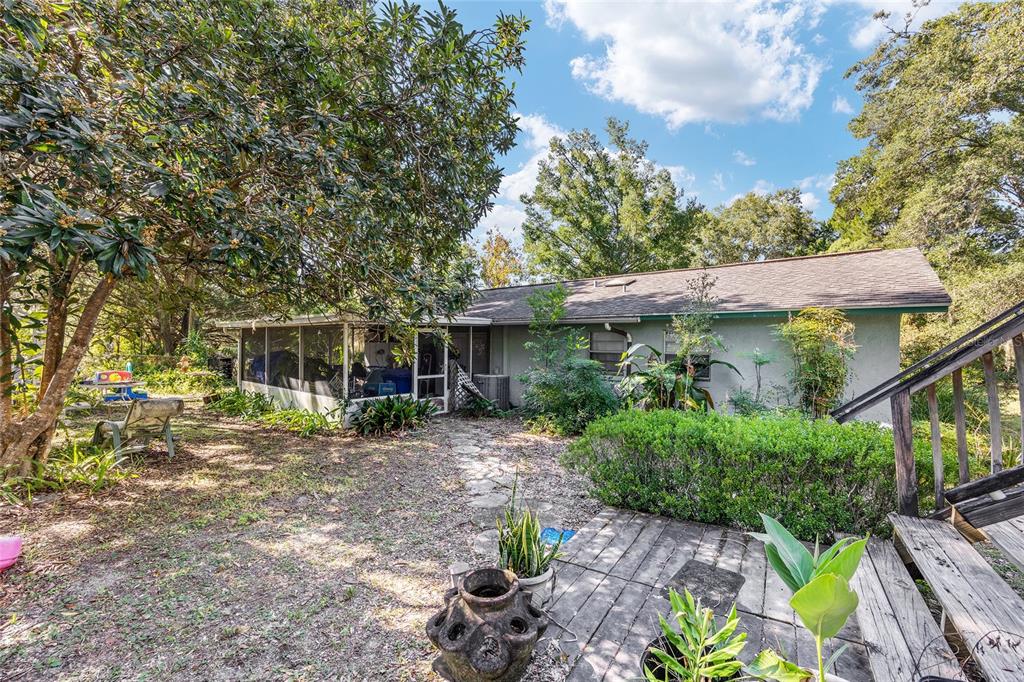A backyard view of a single-story house with a screened porch and wooden deck stairs — 5985 W GULF TO LAKE HIGHWAY, CRYSTAL RIVER, FL