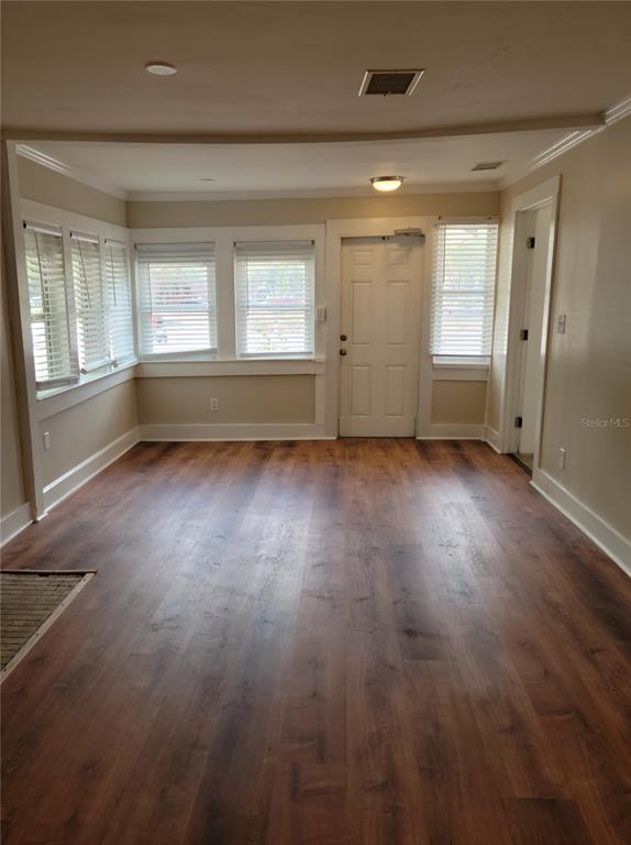 An empty room with wood-look flooring, white trim, multiple windows with blinds, and a door — 1775 FRUITVILLE ROAD, SARASOTA, FL