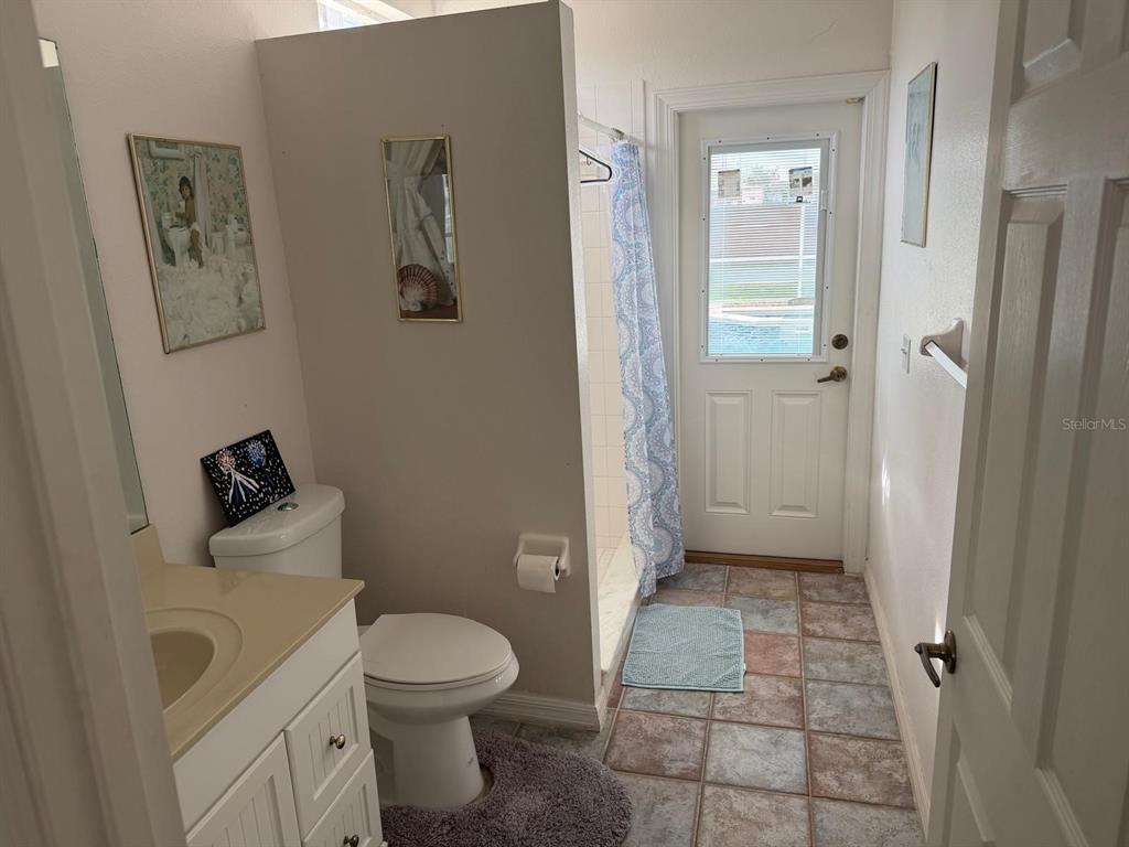 A bathroom with a vanity, toilet, walk-in shower, and a door leading to the outdoors — 471 HOLBORN LOOP, DAVENPORT, FL