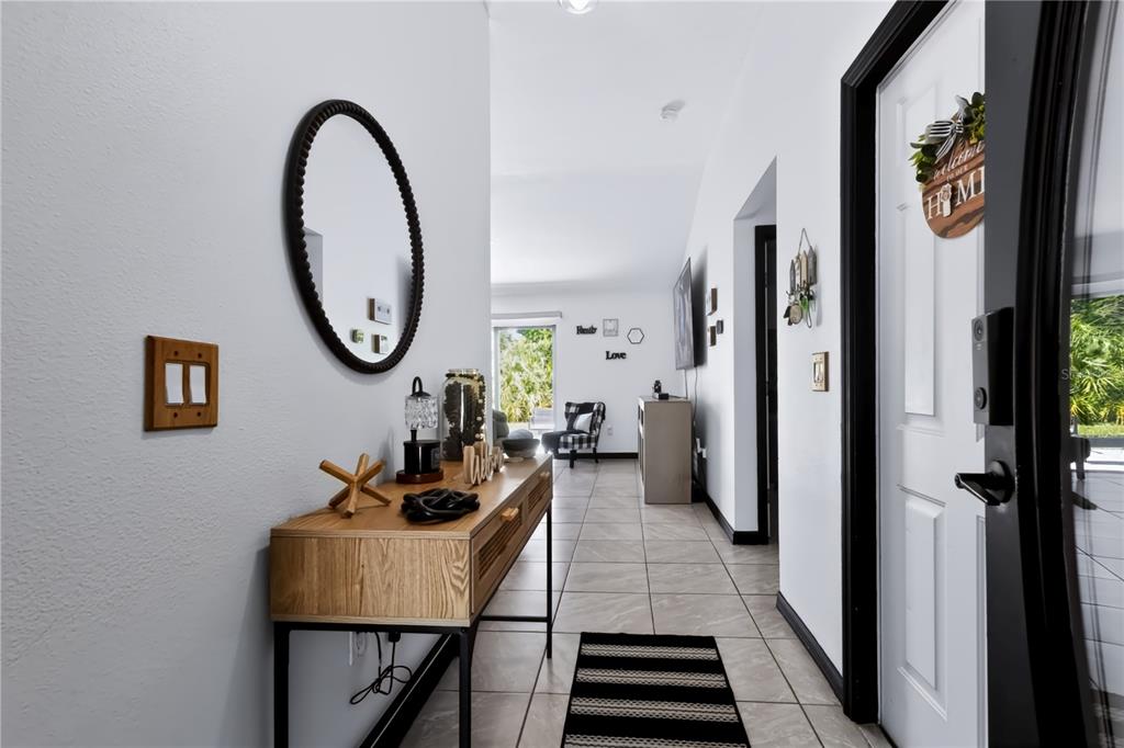 A bright entryway features a wooden console table, a round mirror, and tile flooring — 124 PIERCE STREET, LAKE WALES, FL