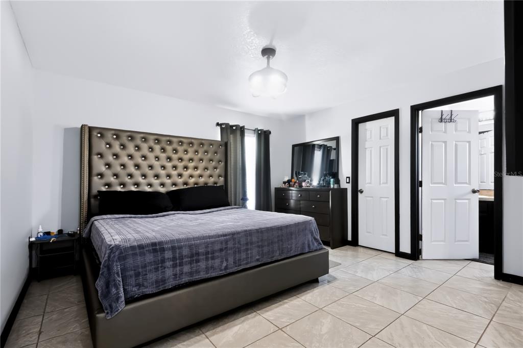 A bedroom features a tufted headboard, tile flooring, and two white doors with black trim — 124 PIERCE STREET, LAKE WALES, FL