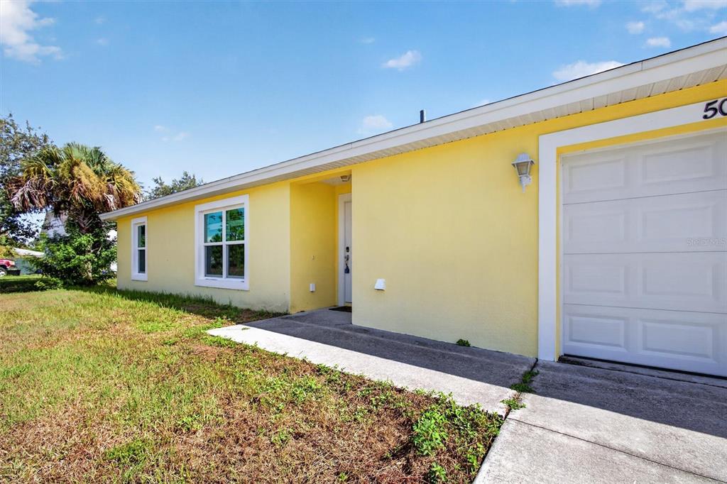 A yellow house exterior features a white garage door, a front entrance, and two windows — 5008 S OBISPO CIRCLE, LABELLE, FL