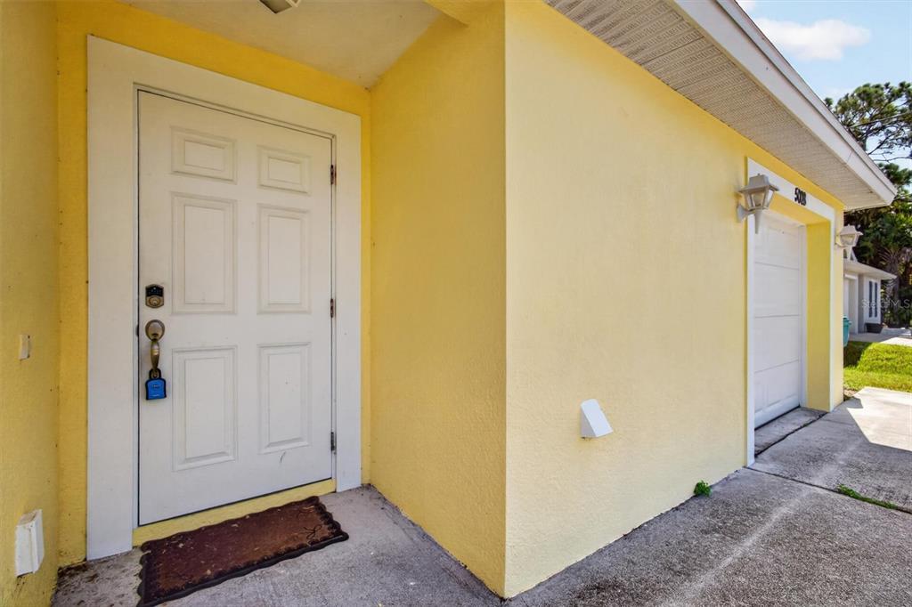 A yellow exterior wall features a white front door and an adjacent garage door — 5008 S OBISPO CIRCLE, LABELLE, FL
