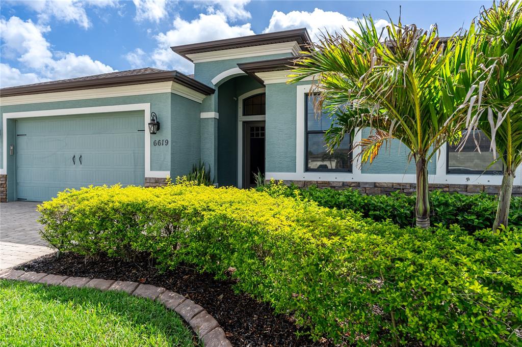 A teal single-story house with a two-car garage, stone accents, and a landscaped front yard — 6619 35TH COURT E, SARASOTA, FL
